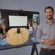 A photo of a man standing next to a TV that shows the preview of what the virtual office will look like